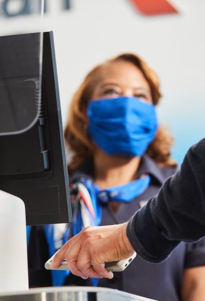 A passenger scans his digital boarding pass at the gate while an American Airlines employee greets and welcomes him onboard
